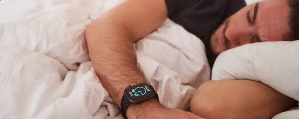 Man Asleep In Bed Wearing Smart Watch As Sun Breaks Through Curtains