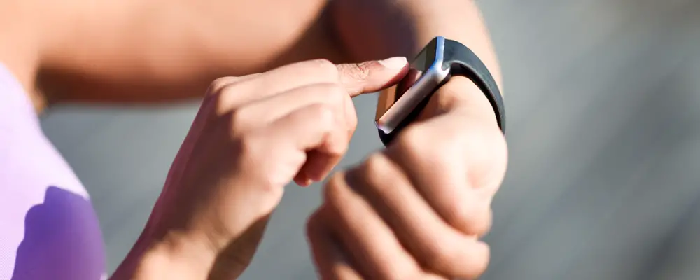 Woman using smartwatch touching touchscreen in active sports activity. Close-up of hands and wrist with smart watch screen.