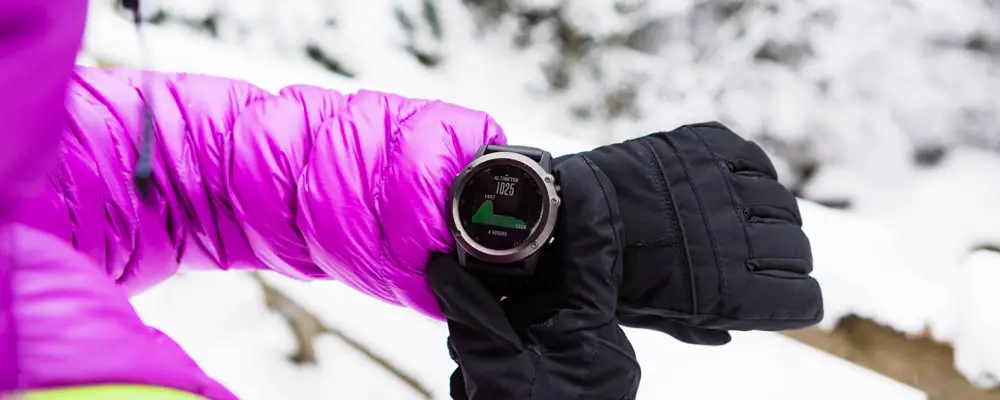 Woman hiker checking the elevation on sports watch, smartwatch with altimeter app in winter woods and mountains. Female trekker trekking in white snowy forest with electronics wearable technology.